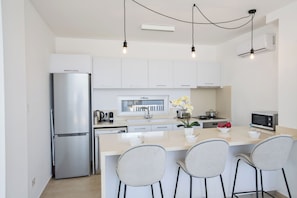 A modern kitchen with a stainless steel refrigerator, a microwave, a sink, and a bar area with three chairs.