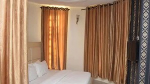 A hotel room with a bed, curtains, a TV, and a wall-mounted light fixture. - Room-waxride Residence - Guest Room (Abuja)