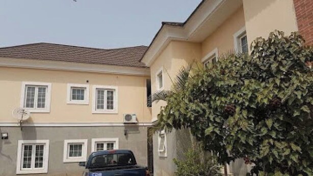 A two-story building with a car parked in front, a tree in the foreground, and a clear sky. - Room-waxride Residence - Guest Room (Abuja)