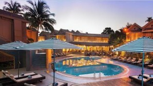 A pool area with lounge chairs and umbrellas, surrounded by buildings with warm lighting. - Room-whispering Palms Resort-guest Room (Lagos)