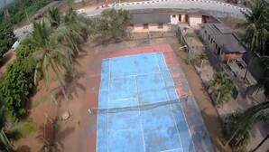 An outdoor tennis court surrounded by greenery and buildings. - Room-whispering Palms Resort-guest Room (Lagos)