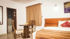 A hotel room with a bed, a desk, a chair, and a window with curtains. - Room-whispering Palms Resort-guest Room (Lagos)