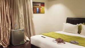 A hotel room with a bed, a small air conditioning unit, a refrigerator, and a painting on the wall. - Room-world Lilies Hotel-guest Room (Ibadan)