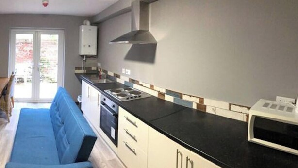 Uma cozinha compacta com sofá, mesa de jantar e televisão fixada na parede.