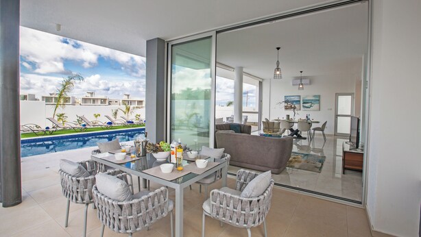 A modern living room with a glass door leading to a balcony overlooking a pool and a cityscape. - Villa Prol26, Stunning 3bdr Protaras Villa With Pool, Close to Fig Tree Bay (Paralimni)