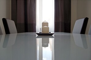 Een vergadertafel met een kaars als middelpunt, twee stoelen en een raam met gordijnen.