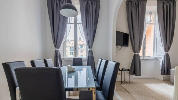 Un comedor moderno con mesa de vidrio, sillas negras y cortinas grises.