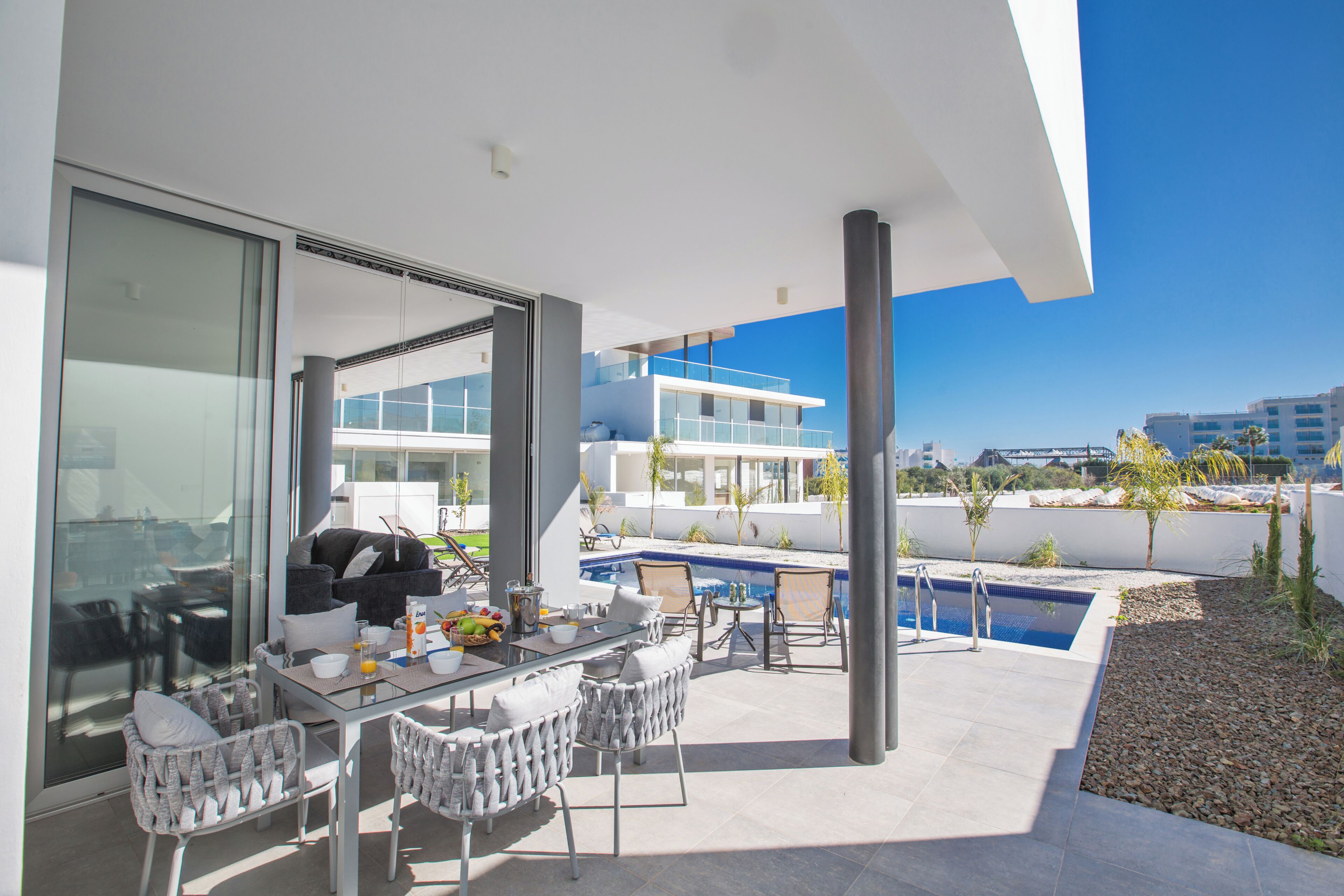 Un área de comedor exterior moderna con piscina y vistas a la ciudad.