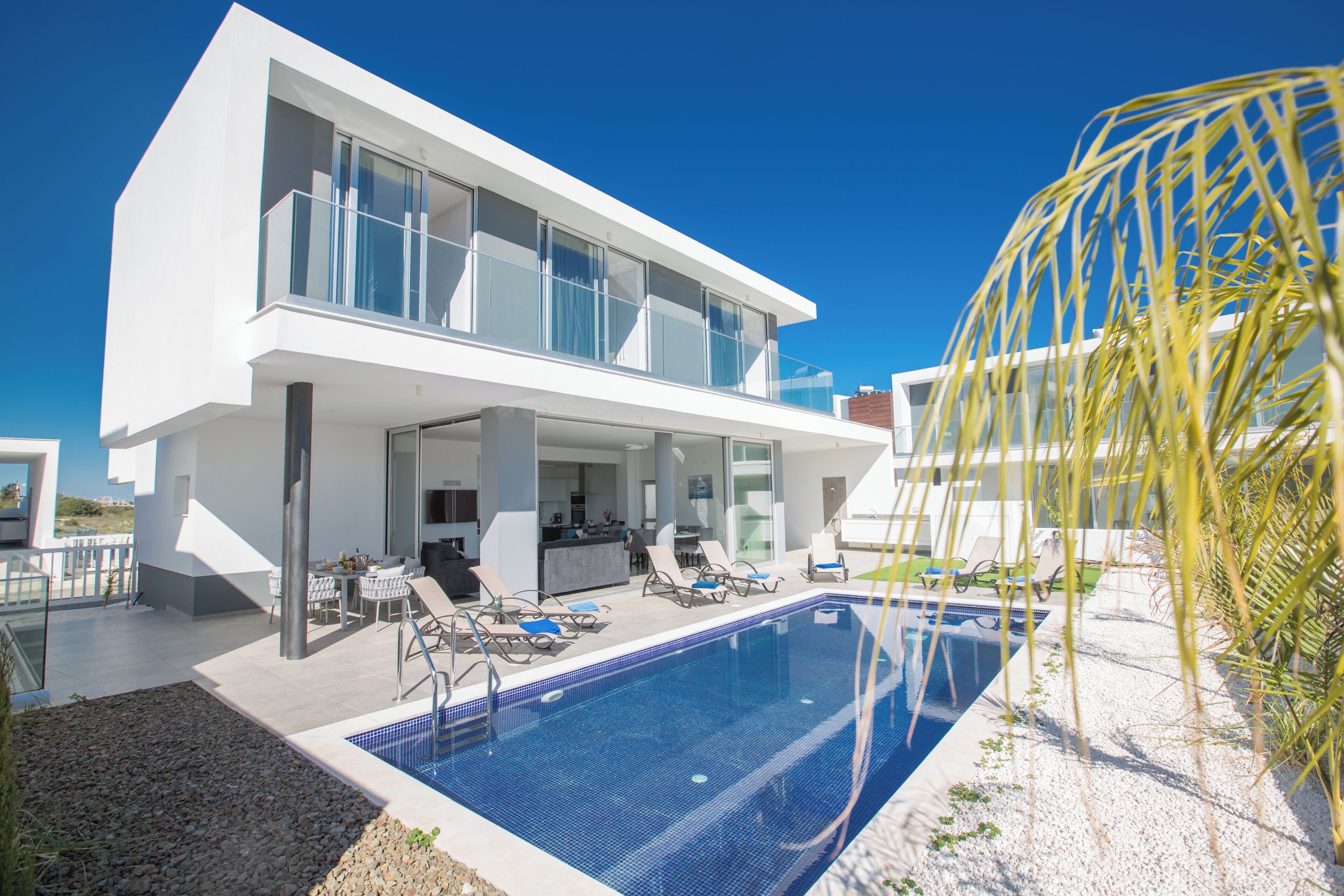 A modern two-story house with a swimming pool, outdoor seating, and a clear blue sky.