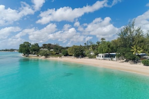 Ein Strand mit klarem türkisblauem Wasser, sandigem Ufer und einem Gebäude mit einem Balkon mit Blick auf das Meer.
