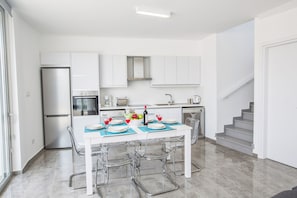 A modern kitchen with white cabinets, a stainless steel refrigerator, and a dining table set with blue placemats and red wine glasses.
