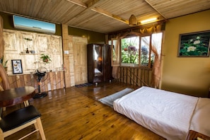 A wooden-floored room with a bed, a table, and a chair.