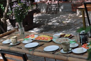 A bamboo table set with plates, bowls, and a vase of flowers.