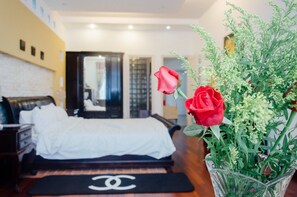 A hotel room with a bed, a Chanel-branded mat, and a vase with red roses and greenery. - Hillside Homestay Hue - Mansion Room (Hue)