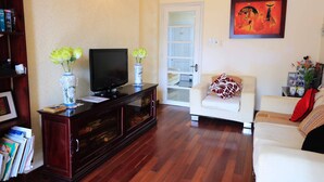 A living room with a TV on a wooden cabinet, a white sofa, and a door with glass panels.