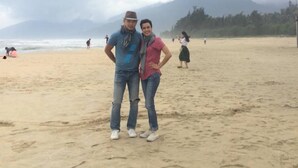 A beach with a couple standing in the foreground, a sandy beach, and mountains in the background. - Hillside Homestay Hue - Silk Room (Hue)