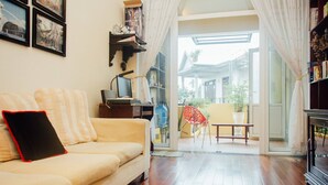 A living room with a sofa, a TV, and a bookshelf. There is a sliding glass door leading to an outdoor area with a bench and plants. - Hillside Homestay Hue - Silk Room (Hue)