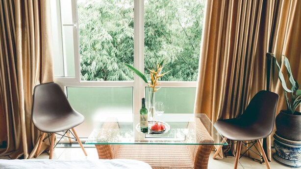 A room with a glass table, two chairs, a bottle, a glass, and a plate with a fruit. - Hillside Homestay Hue - Triple Room top Apartment (Hue)