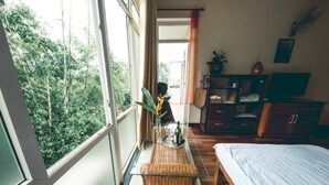 A room with a bed, a small table with a vase and a bottle, a wardrobe, and a window with a view of greenery. - Hillside Homestay Hue - Triple Room top Apartment (Hue)