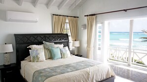 A bedroom with a large bed, two bedside tables, a nightstand, a window with curtains, and a view of the ocean. - Silver Sands #1 - by Zenbreak (Silver Sands)