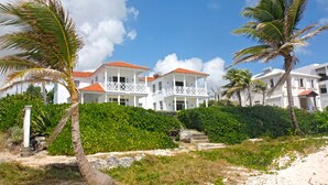 A beachfront property with white buildings, a sandy beach, and palm trees. - Silver Sands #1 - by Zenbreak (Silver Sands)
