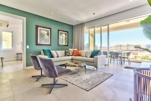 A modern living room with a sectional sofa, a coffee table, and a view of the city through large windows.