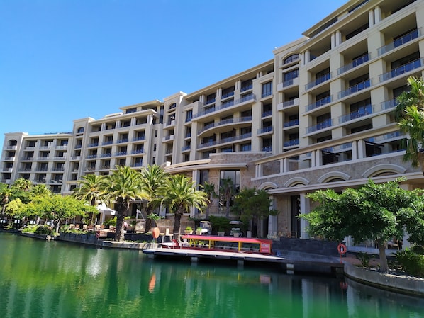 A multi-story hotel with balconies, a water body in front, and a small dock with a boat.