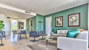 A modern living room with a grey sofa, a coffee table, and a dining area with chairs and a table. - Luxury Three Bedroom Apartment - Fully Furnished and Equipped (Cape Town)
