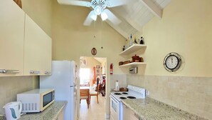 A kitchen with a microwave, stove, and sink. There is a ceiling fan, a clock on the wall, and a fire extinguisher. - The Gem - by Zenbreak (Apple Hall)