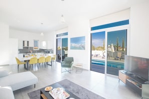 A modern living room with a dining area, a TV, and a pool view.