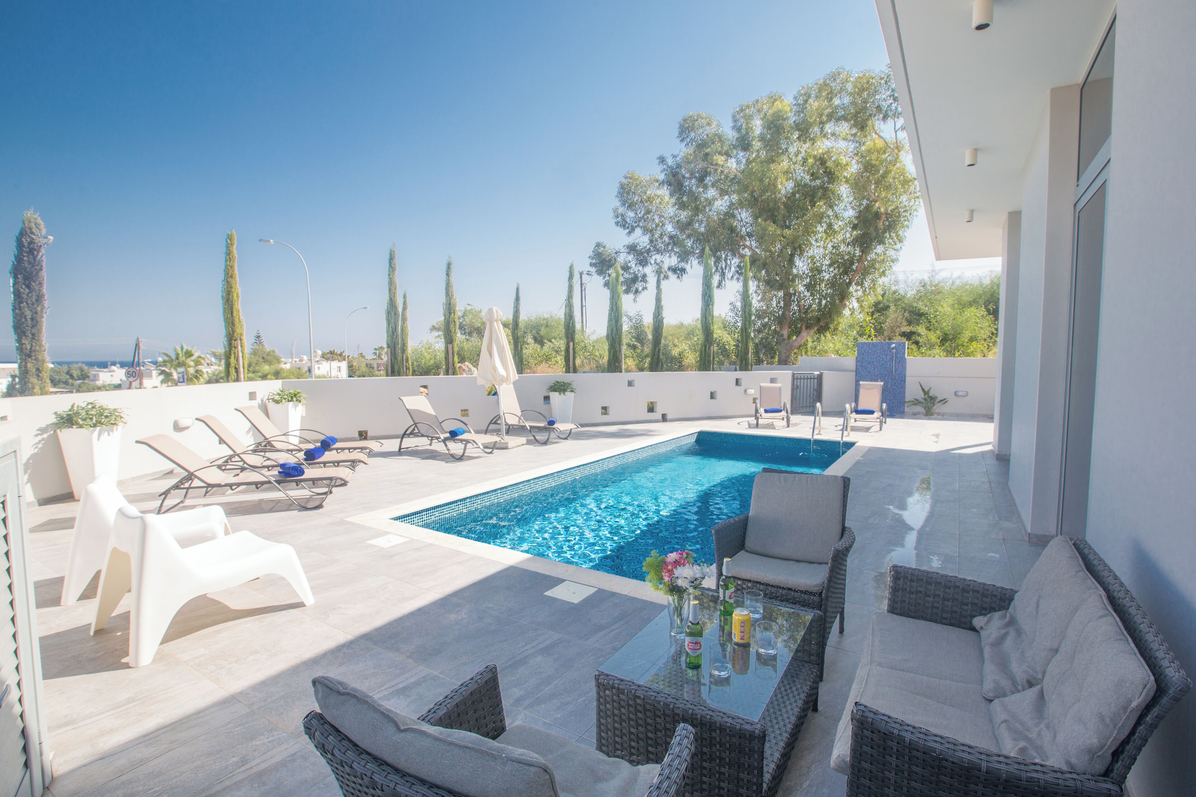 A rooftop pool area with lounge chairs, a table with drinks, and a view of the sea.