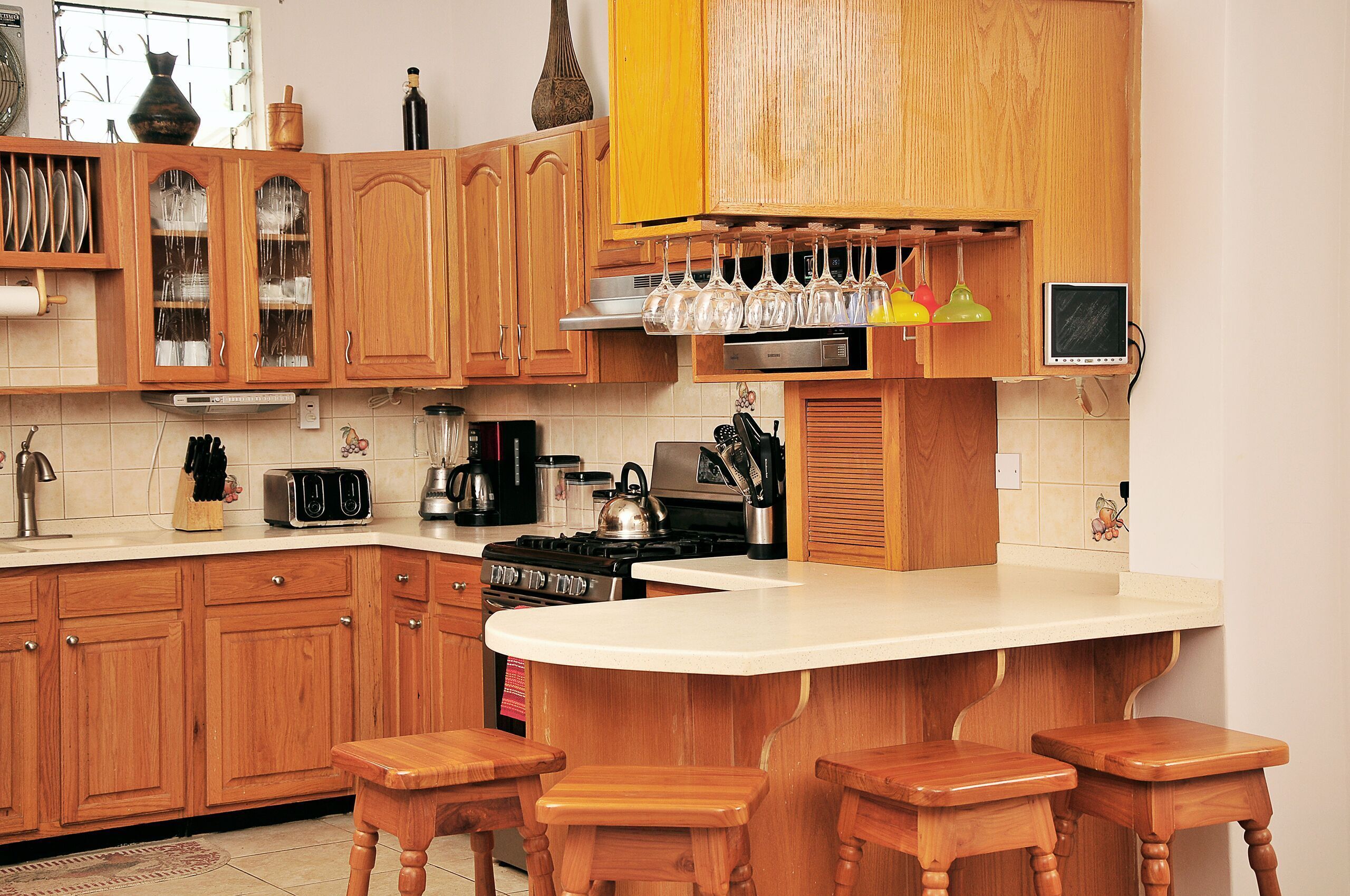 Een keuken met houten kastjes, een fornuis, een spoelbak en een bar met barkrukken.