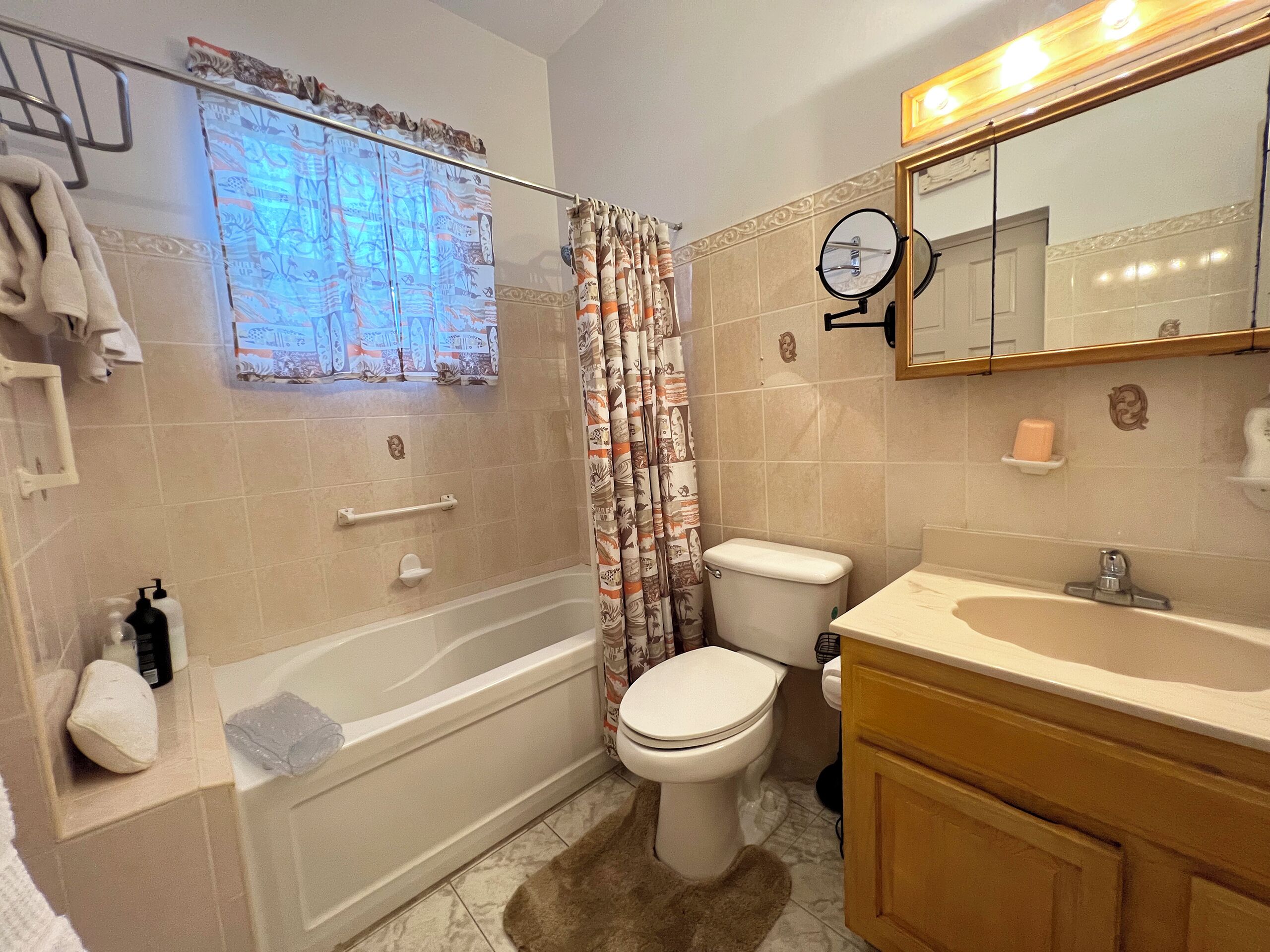 A bathroom with a bathtub, toilet, and sink. There is a towel rack, a mirror, and a window with curtains.