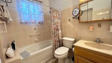 A bathroom with a bathtub, toilet, and sink. There is a towel rack, a mirror, and a window with curtains.