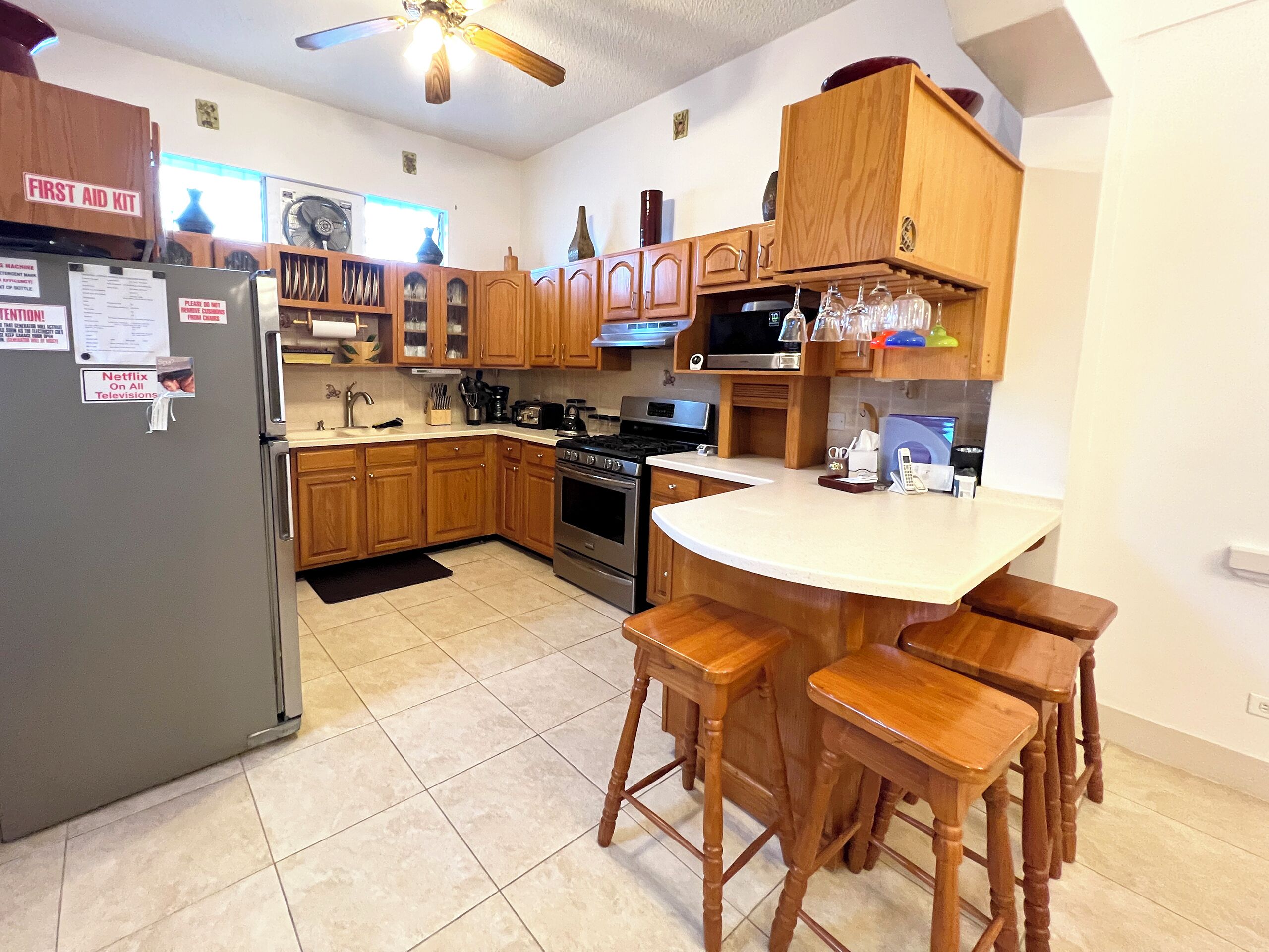A kitchen with wooden cabinets, a refrigerator, a stove, and a bar area with stools.