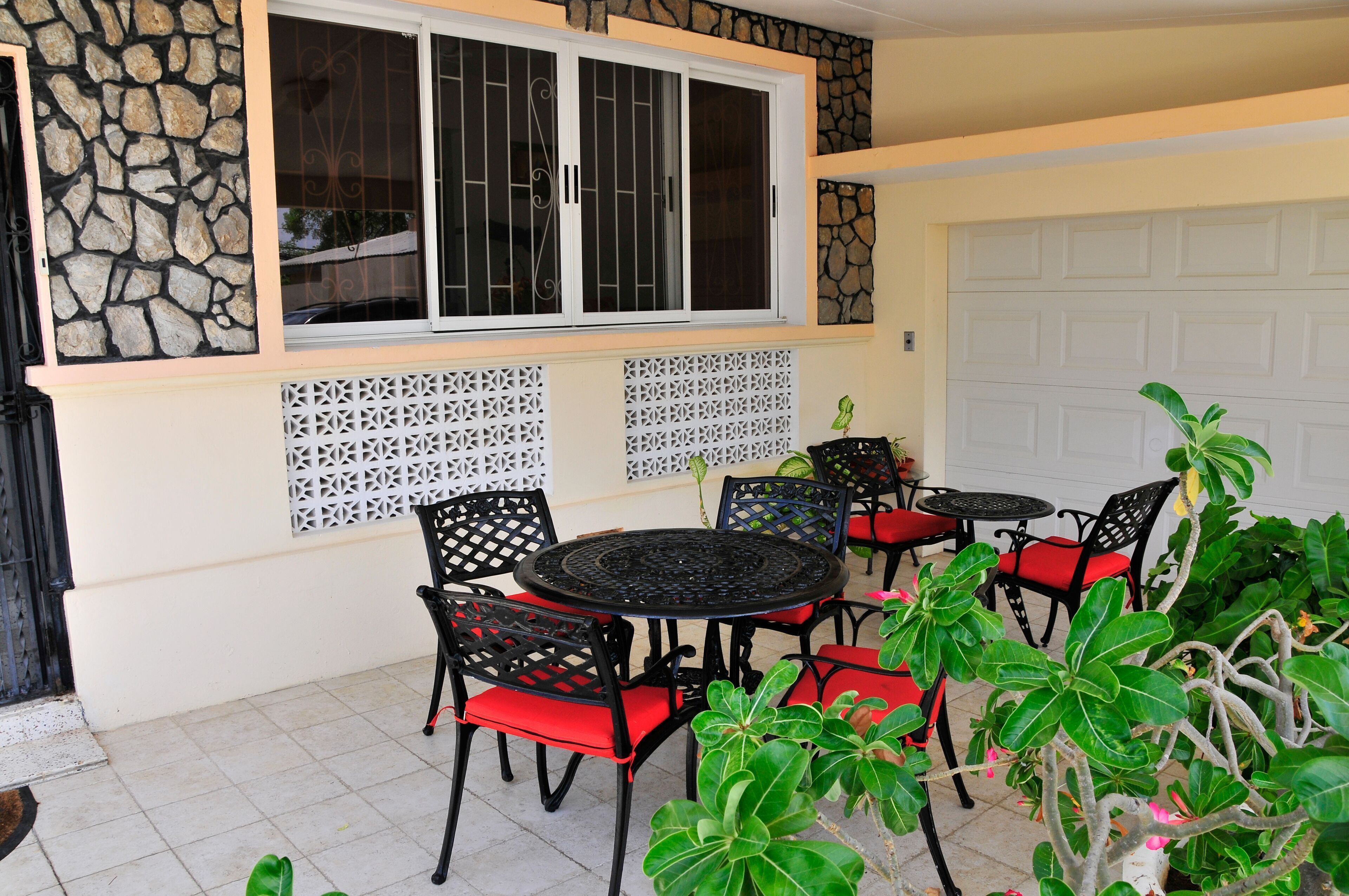 An outdoor patio with a stone wall, a white garage door, and a black metal table with red cushions.