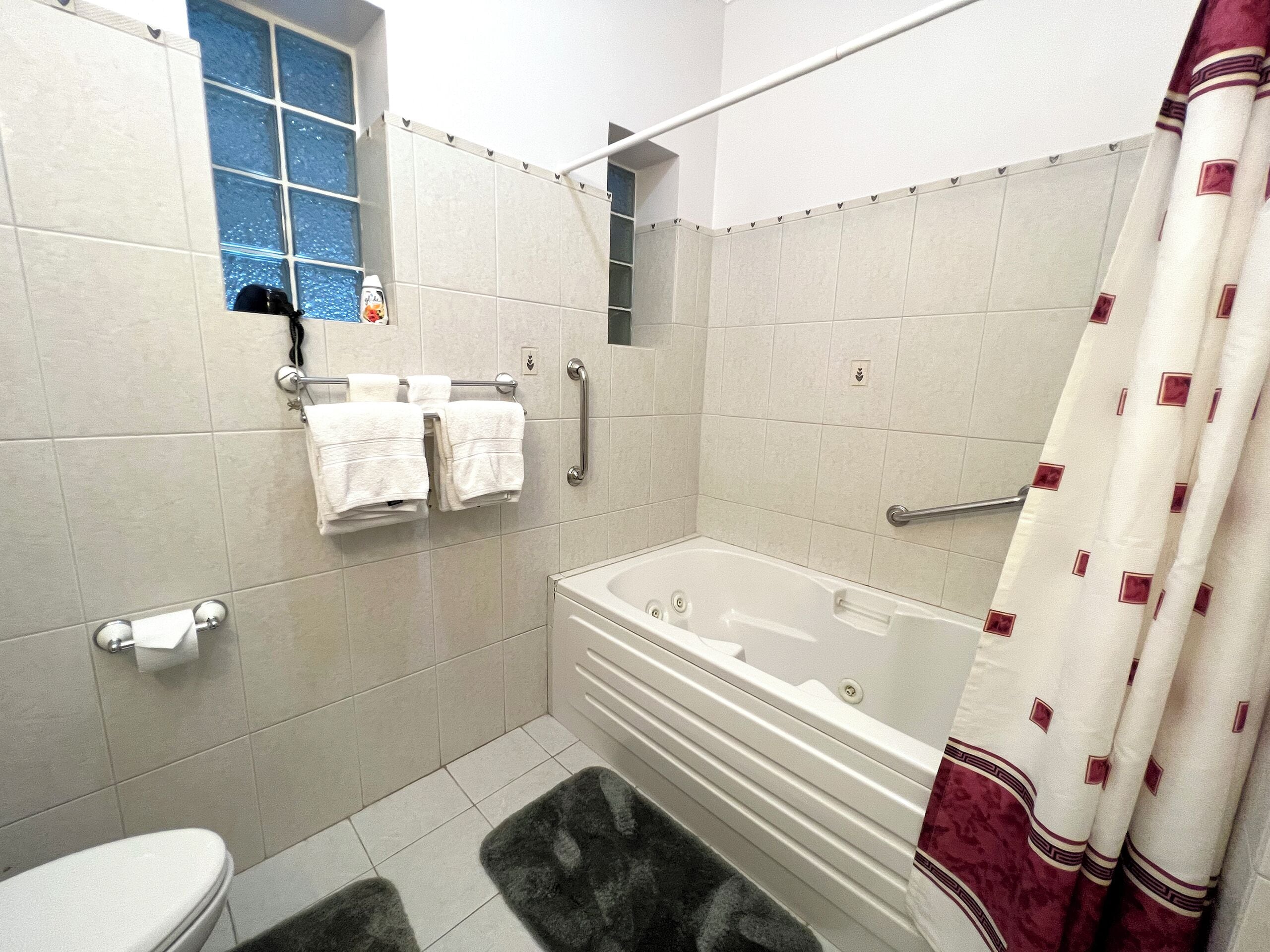 A bathroom with a bathtub, a toilet, a shower curtain, and a window.