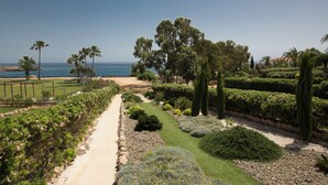 A landscaped garden with a pathway, various plants, and a view of the ocean. - Protaras Mesogeios Villa Me16 Beachfront Villa in Protaras Center (Paralimni)