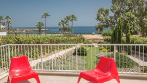 A balcony with two red plastic chairs, a white railing, and a view of the sea and greenery. - Protaras Mesogeios Villa Me16 Beachfront Villa in Protaras Center (Paralimni)