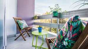 Un balcon avec une chaise en bois, une petite table ronde et deux plantes en pot.