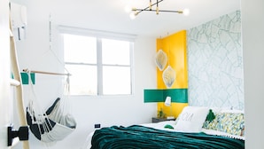 Une chambre à coucher avec un lit, un fauteuil suspendu, une fenêtre et un mur orné d’un motif de feuilles.