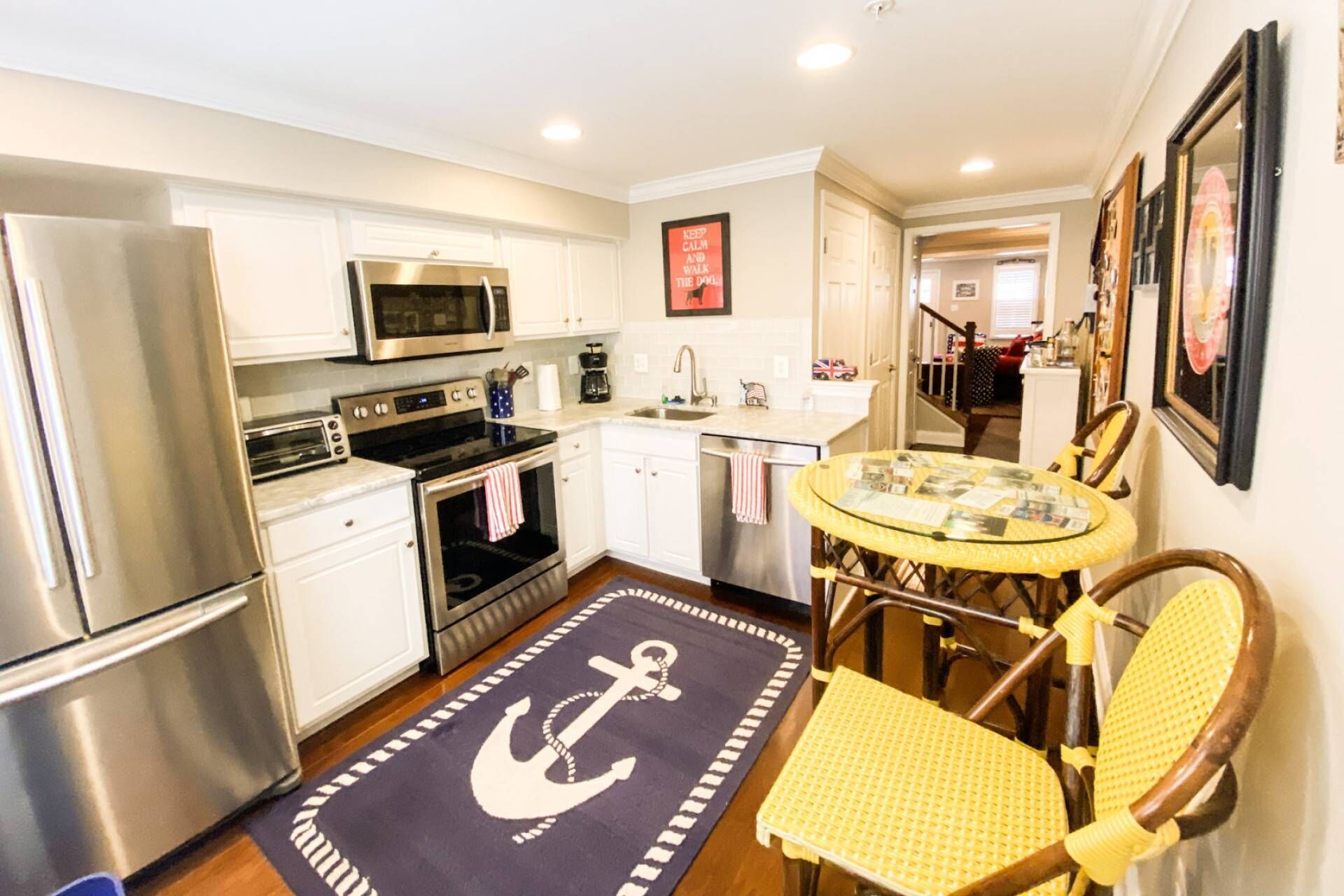 A compact kitchen with stainless steel appliances, a small dining area with a round table and chairs, and a nautical-themed rug.