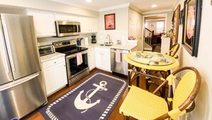 A compact kitchen with stainless steel appliances, a small dining area with a round table and chairs, and a nautical-themed rug. - Go Navy! Steps to USNA, City Dock & Street Parking (Annapolis)