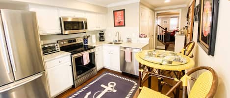 A compact kitchen with stainless steel appliances, a small dining area with a round table and chairs, and a nautical-themed rug.