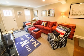 A living room with a red sofa, a navy-themed ottoman, and a chair with a star pattern. - Go Navy! Steps to USNA, City Dock & Street Parking (Annapolis)