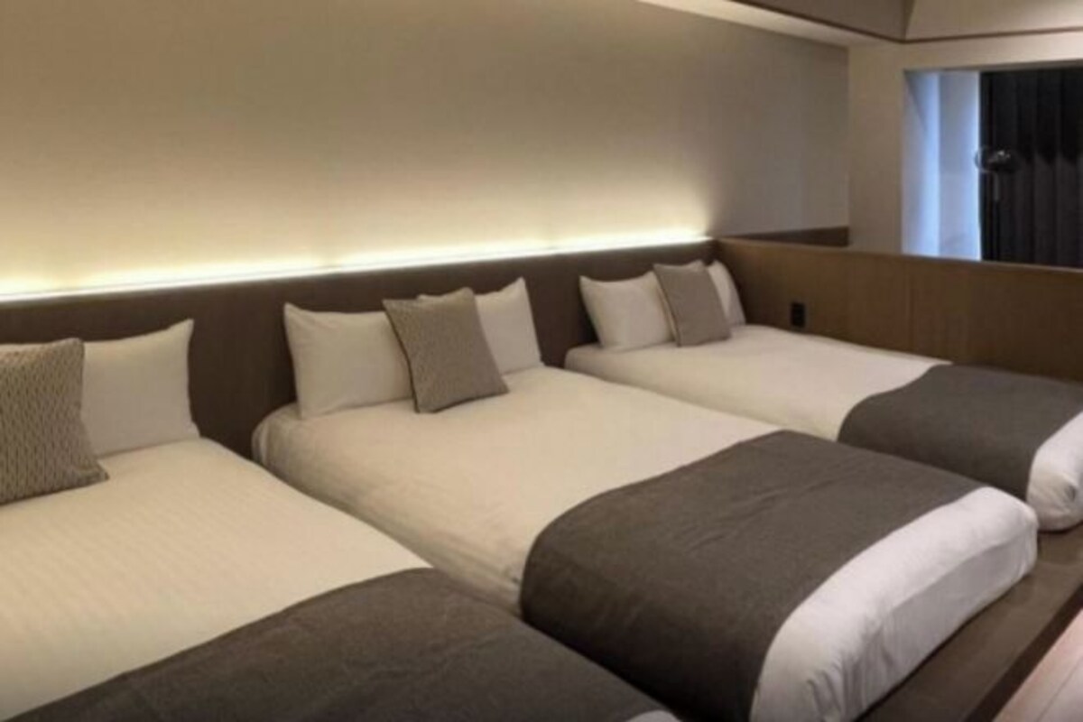 A hotel room with three beds aligned in a row, each with a headboard and pillows.