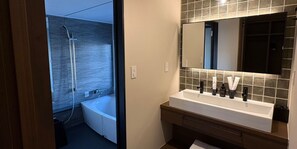 A modern bathroom with a bathtub, a sink with a mirror, and toiletries. - BAND HOTEL HAKATA (Fukuoka)