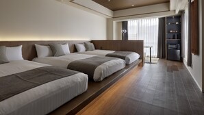 Una habitación de hotel moderna con tres camas, piso de madera y una zona de cocina integrada.
