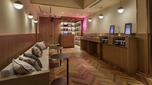 Un vestíbulo de hotel con un mostrador de recepción de madera, una zona de estar con un sofá y mesas redondas, y un suelo con estampado de espiga.