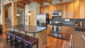 A kitchen with wooden cabinets, a stainless steel refrigerator, a microwave, and a stove. There is a bar area with stools.